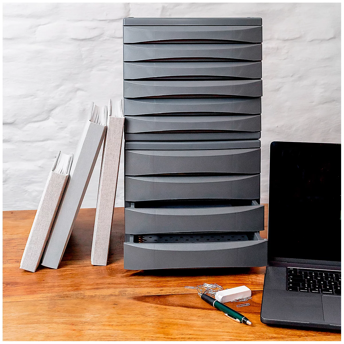 Grey drawer cabinet with an open drawer on wood, next to books and laptop.