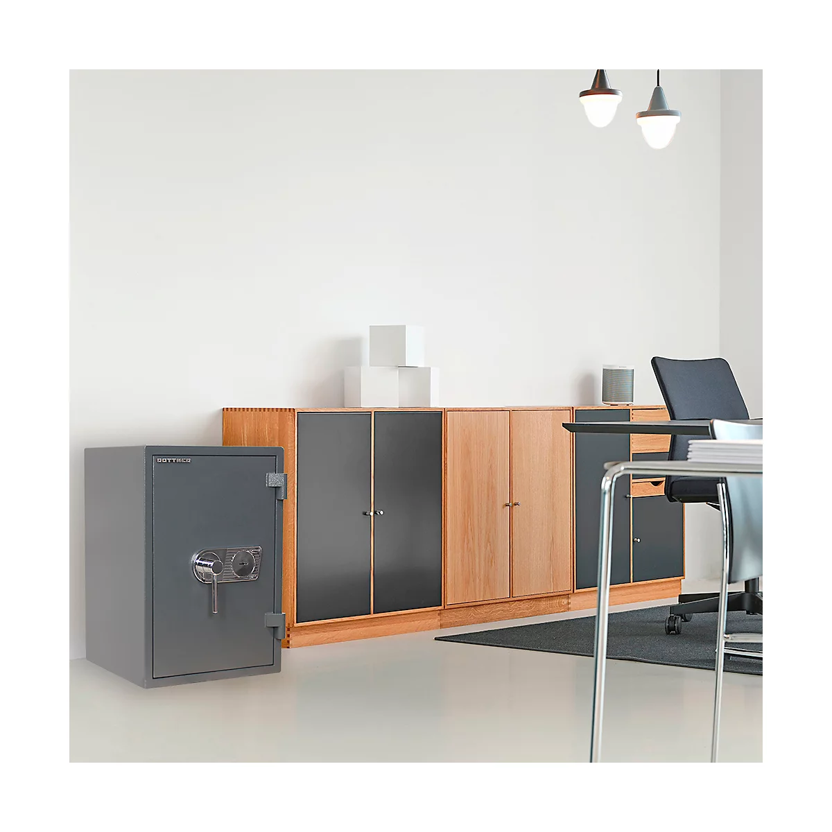 Un coffre-fort gris dans un bureau. Derrière lui se trouvent des armoires, un bureau et une chaise.