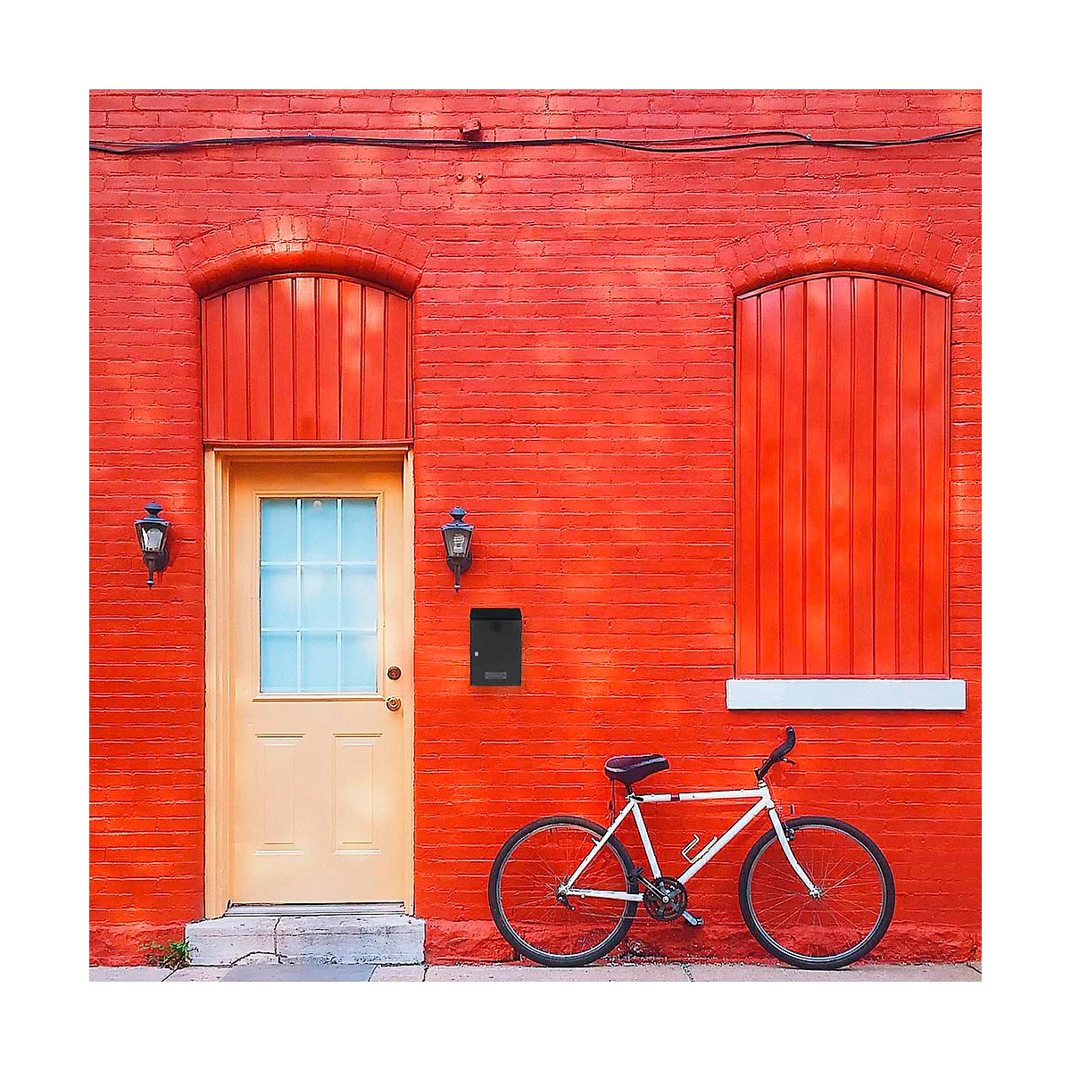 Un mur de briques rouges avec une porte jaune, une fenêtre avec des volets rouges et un vélo devant.
