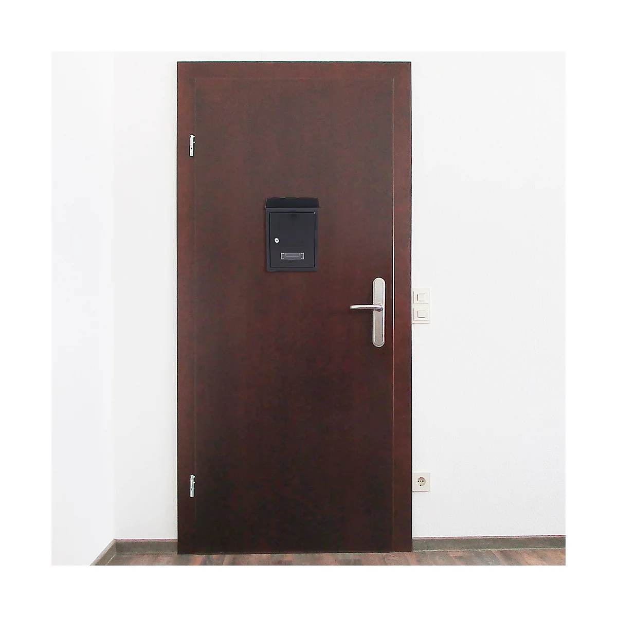 Porte en bois marron avec boîte aux lettres noire, poignée argentée et mur blanc à côté.