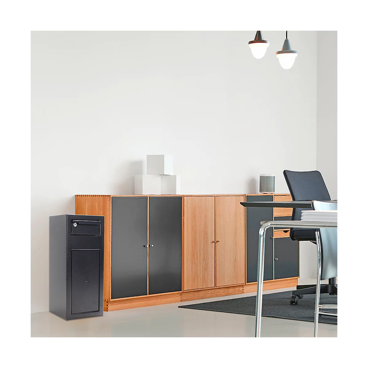 Aménagement de bureau : bureau, chaises, armoires. Coffre-fort noir à gauche. Mur blanc en arrière-plan.