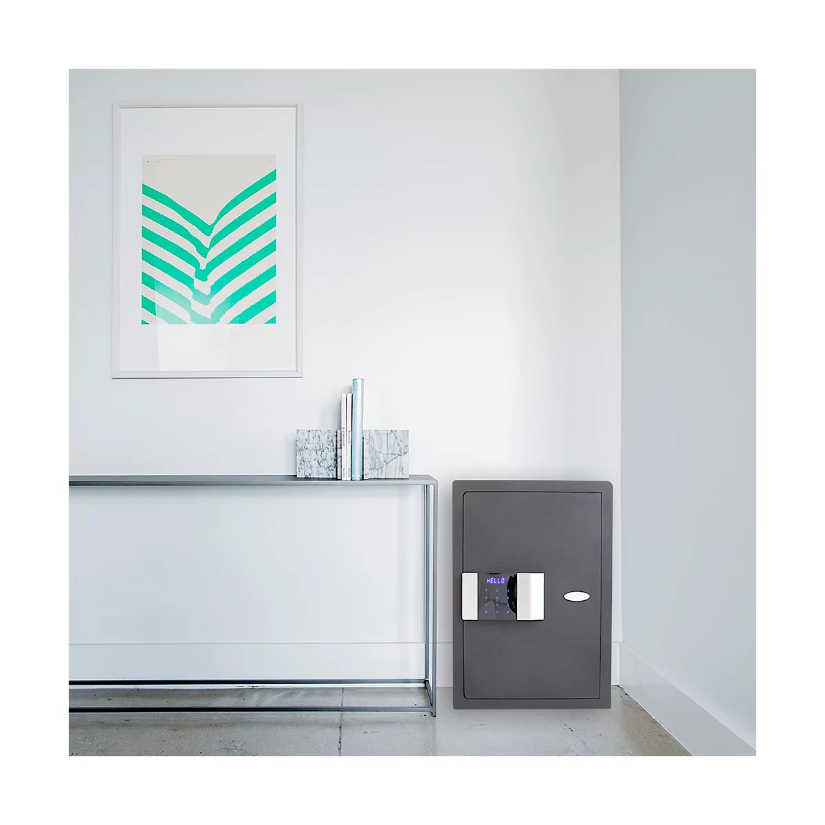 Coffre-fort gris sur mur blanc. Au-dessus d'une console métallique, une image avec des lignes en zigzag vertes est accrochée.