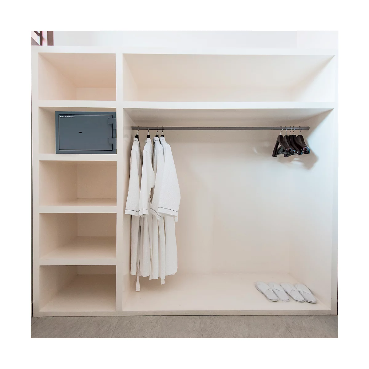 Armoire blanche avec coffre-fort, peignoirs et pantoufles. Étagères et une tringle à vêtements à l'intérieur.