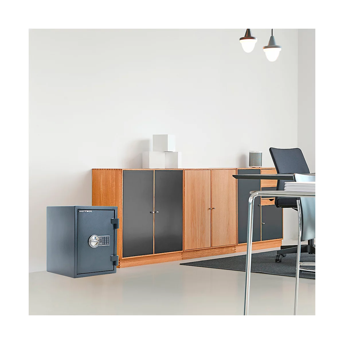 Ein Tresor steht in einem Büro vor einer Schrankwand. Der Tresor ist dunkelblau und hat ein Zahlenschloss. Dahinter Schränke in Holz und dunkler Farbe.