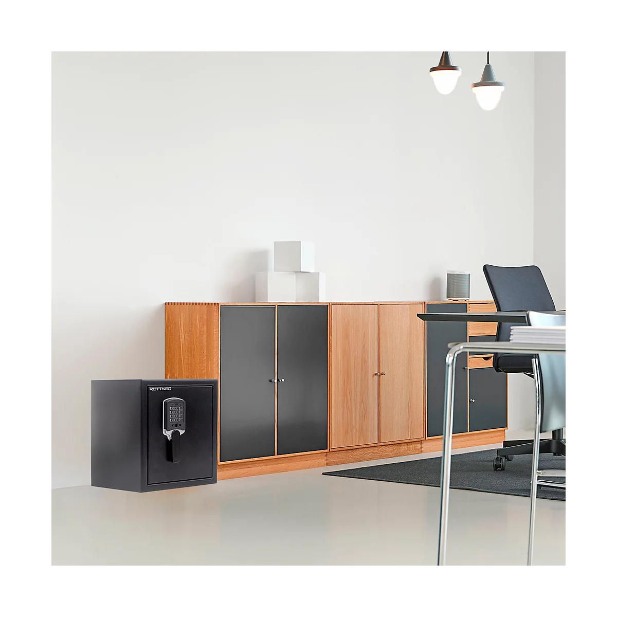 Black safe with digital lock in front of wooden cabinet in modern office. Above, pendant lamps.