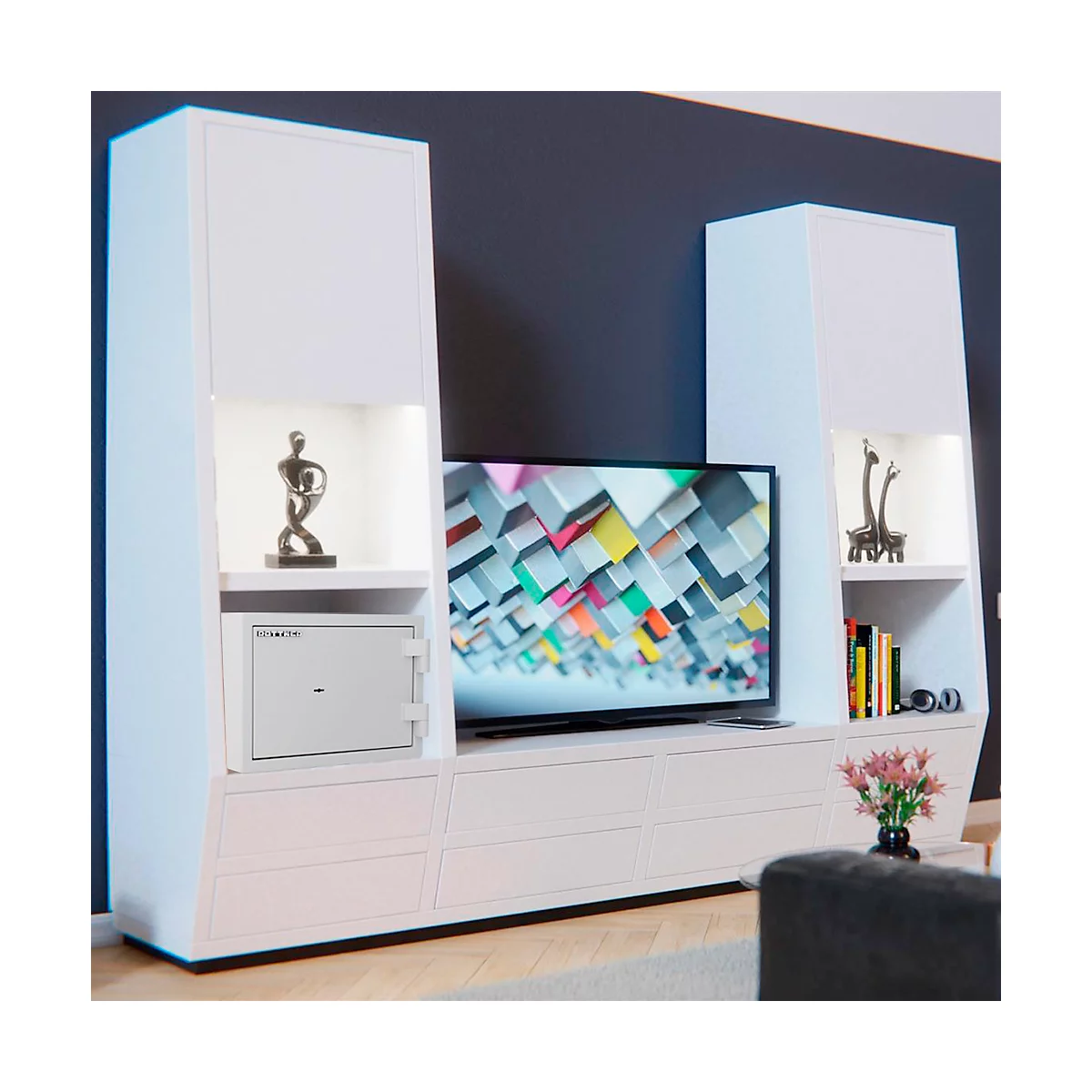 White living room unit with TV. A safe is in a compartment. Decorative figures on the shelves.