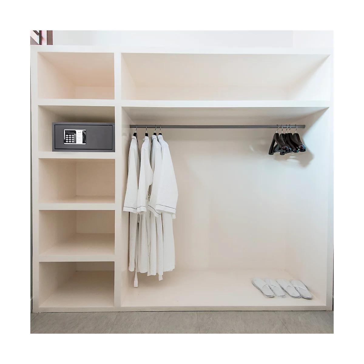 Walk-in closet with safe, bathrobes, hangers, and slippers. Light neutral color scheme.