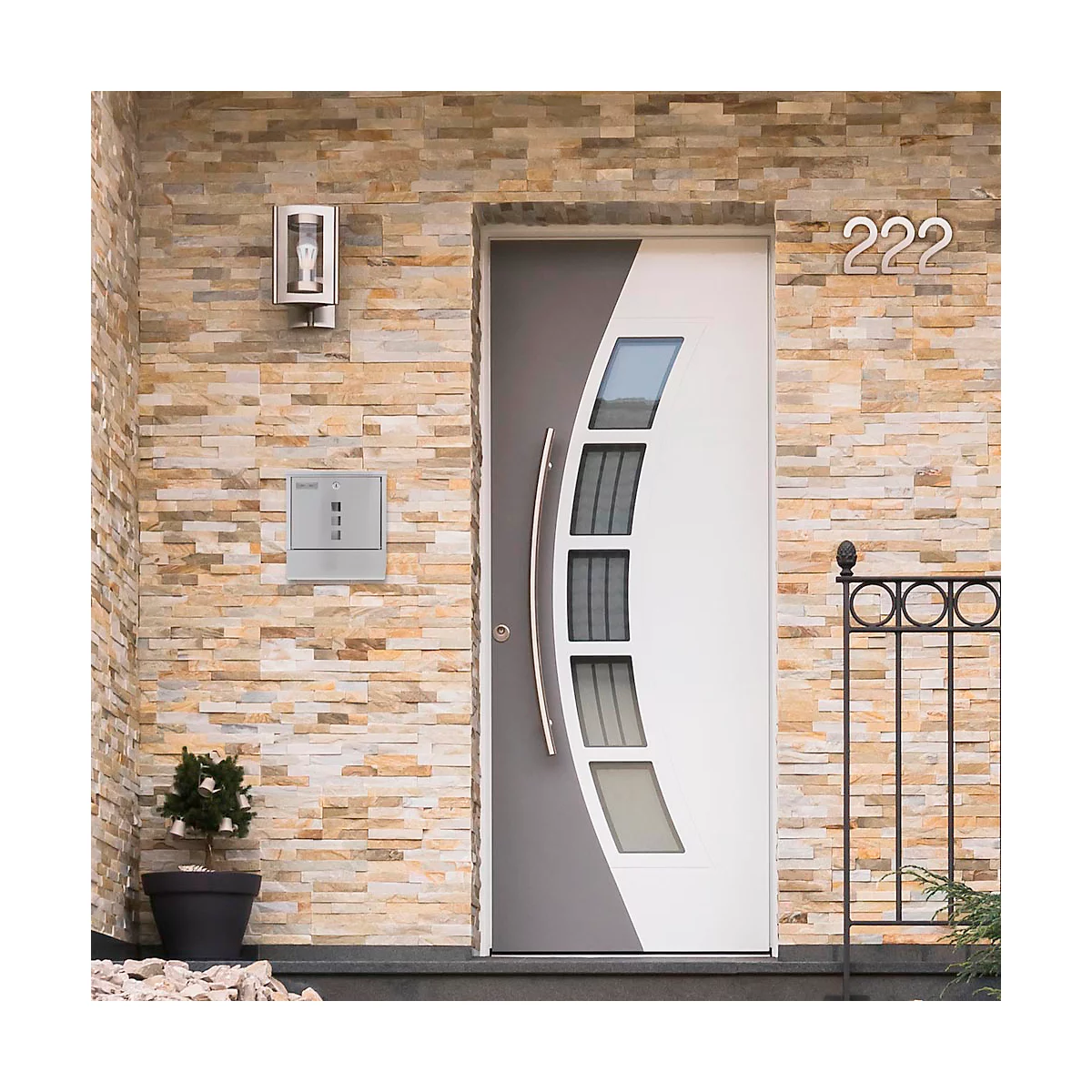 Modern front door, partly grey, partly white. On the wall are a house number 222, a lamp and a mailbox.
