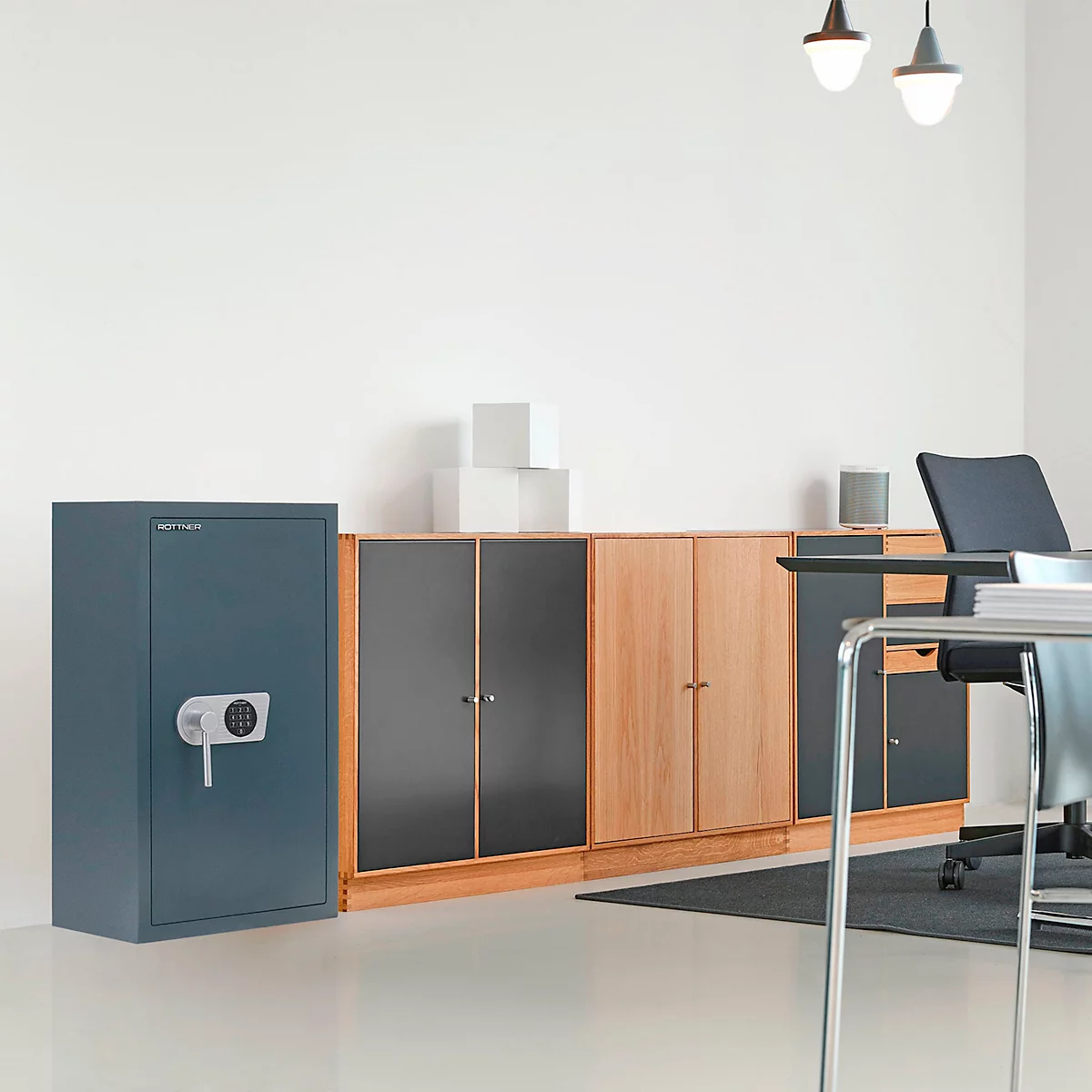 Blue-green safe, next to wooden cabinets. Desk with chair and lamps in the background.
