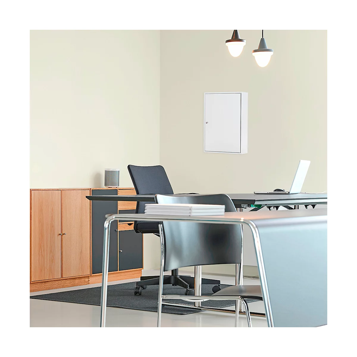 Weißer Sicherungskasten an einer Wand in einem Büro. Schreibtisch mit Laptop und Stuhl im Vordergrund.