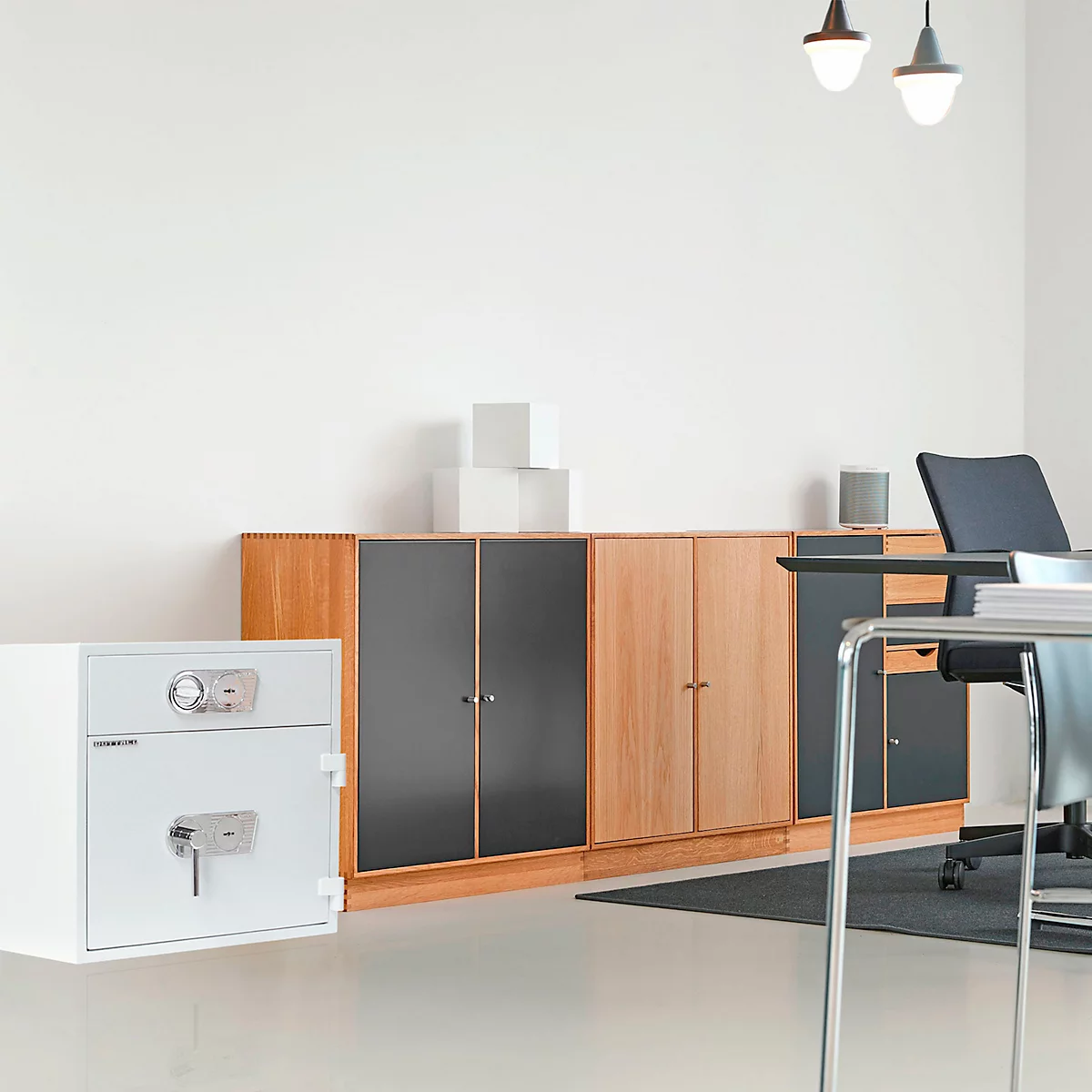 Weisser Tresor, Schränke, Schreibtisch in einem Büro. Zwei Deckenleuchten.