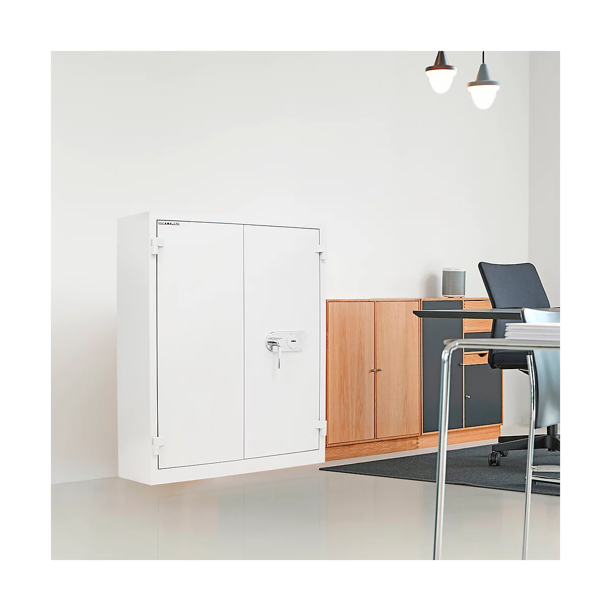 Weißer Tresor mit Schlüssel in einem Büro. Im Hintergrund Schreibtisch, Aktenschrank und Lampen.