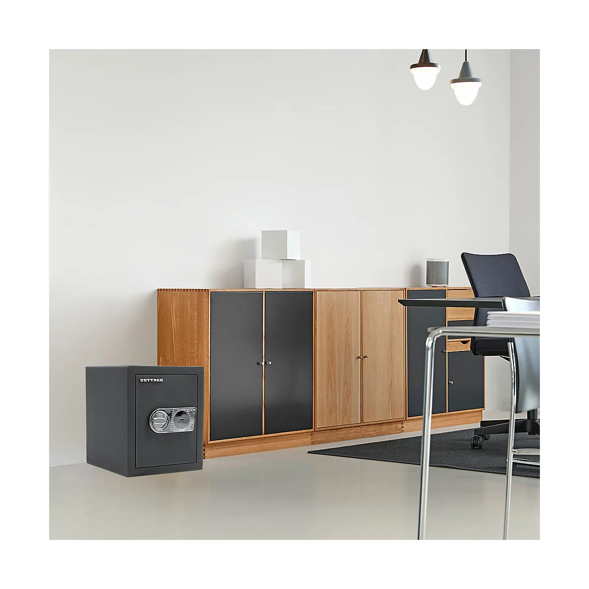Grauer Tresor in einem Büro vor einem Schrank. Rechts ein Schreibtisch und Stuhl.