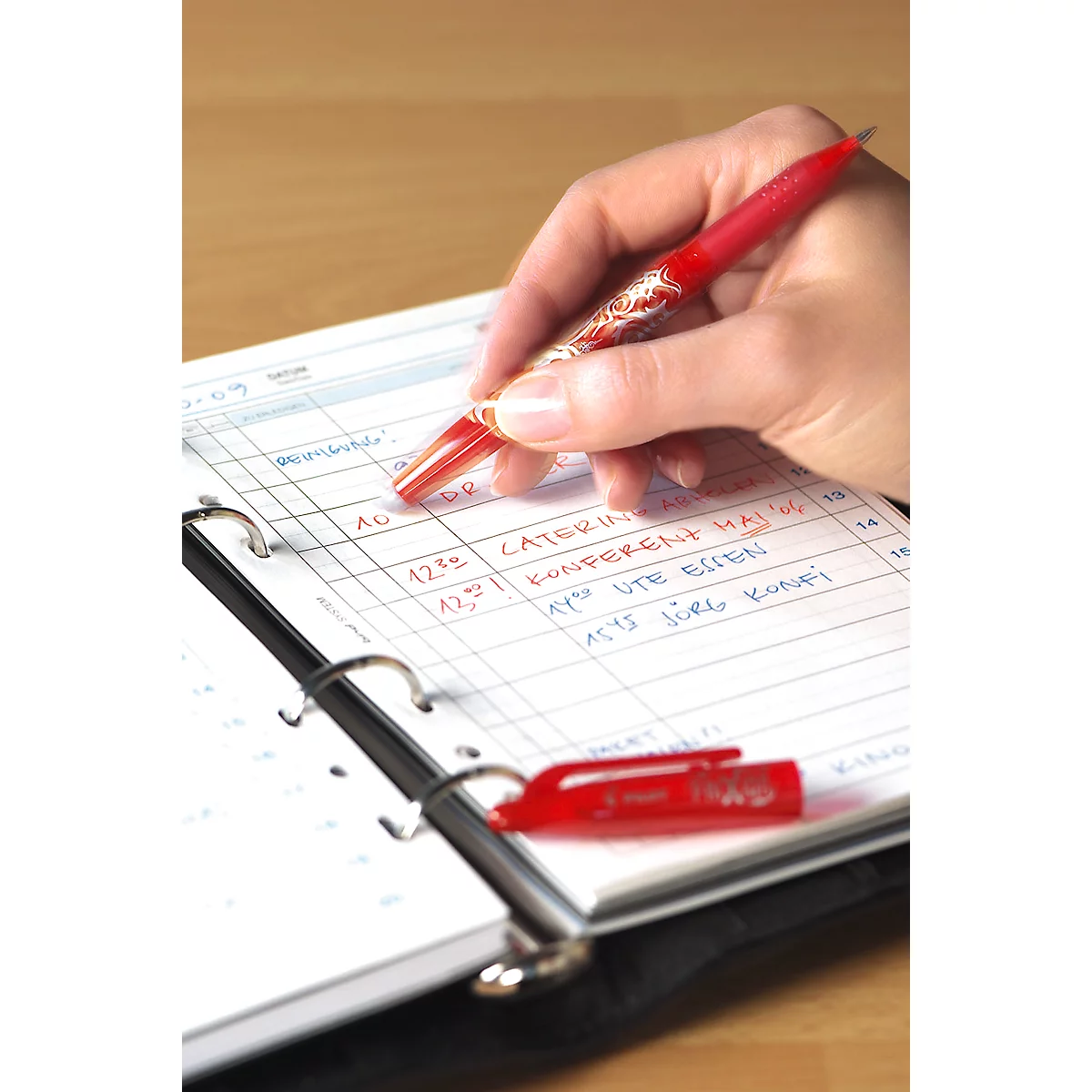 Una mano escribe en un cuaderno con un bolígrafo rojo. El bolígrafo está abierto al lado.