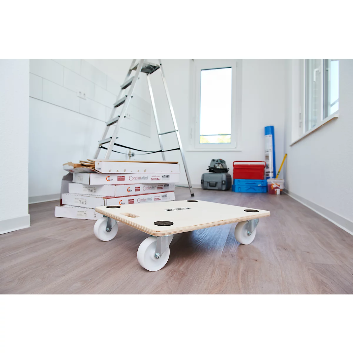 Plateau roulant en bois avec des roues blanches, des outils et des boîtes en arrière-plan.