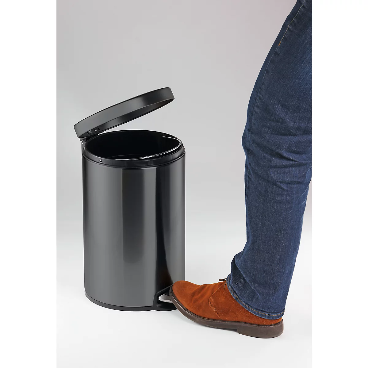 A black trash can with an open lid. A foot is pressing the pedal.