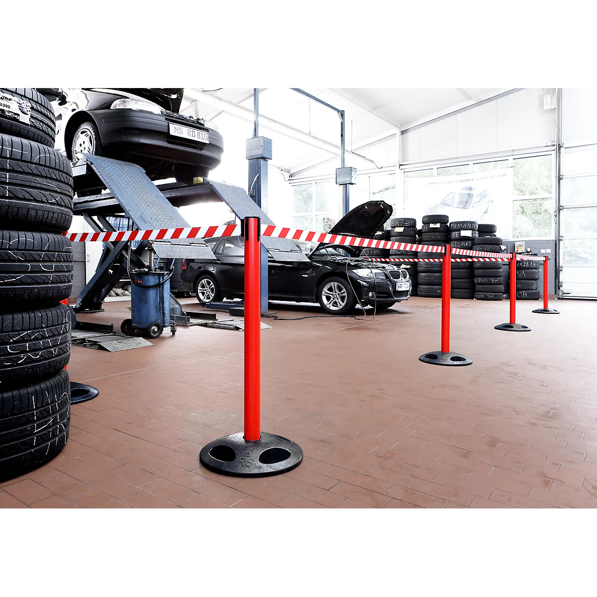 Workshop with vehicles on hoists, stacks of tires and barrier tapes. Red posts with red and white barrier tape.