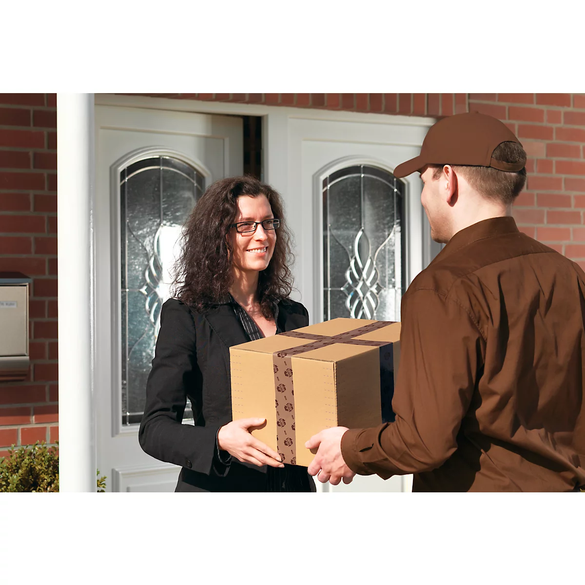 Un livreur remet un colis à un client à la porte d'entrée. La femme sourit.