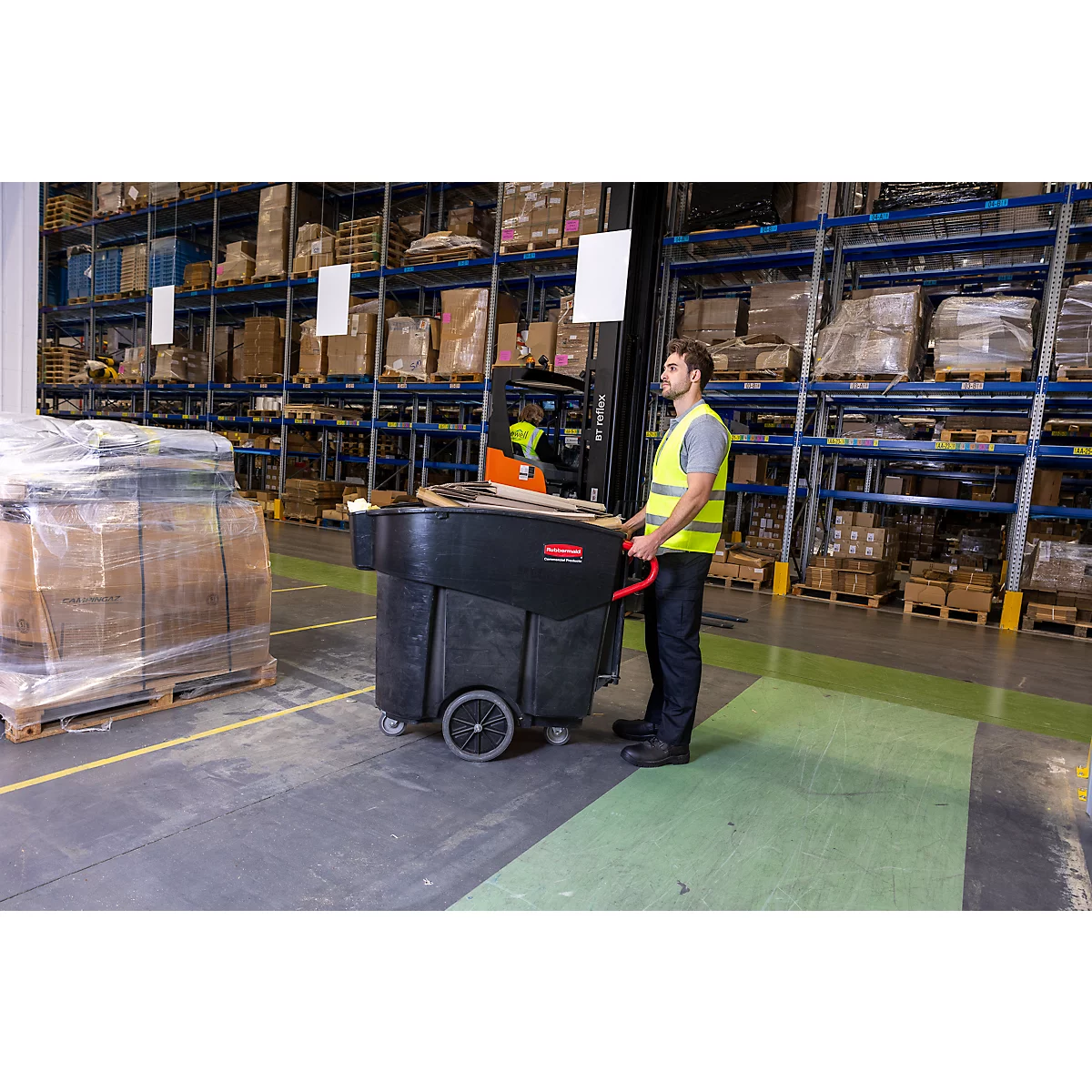 Een man in een magazijn duwt een zwarte transportwagen. Rechts staat een vorkheftruck, op de achtergrond staan opslagrekken.