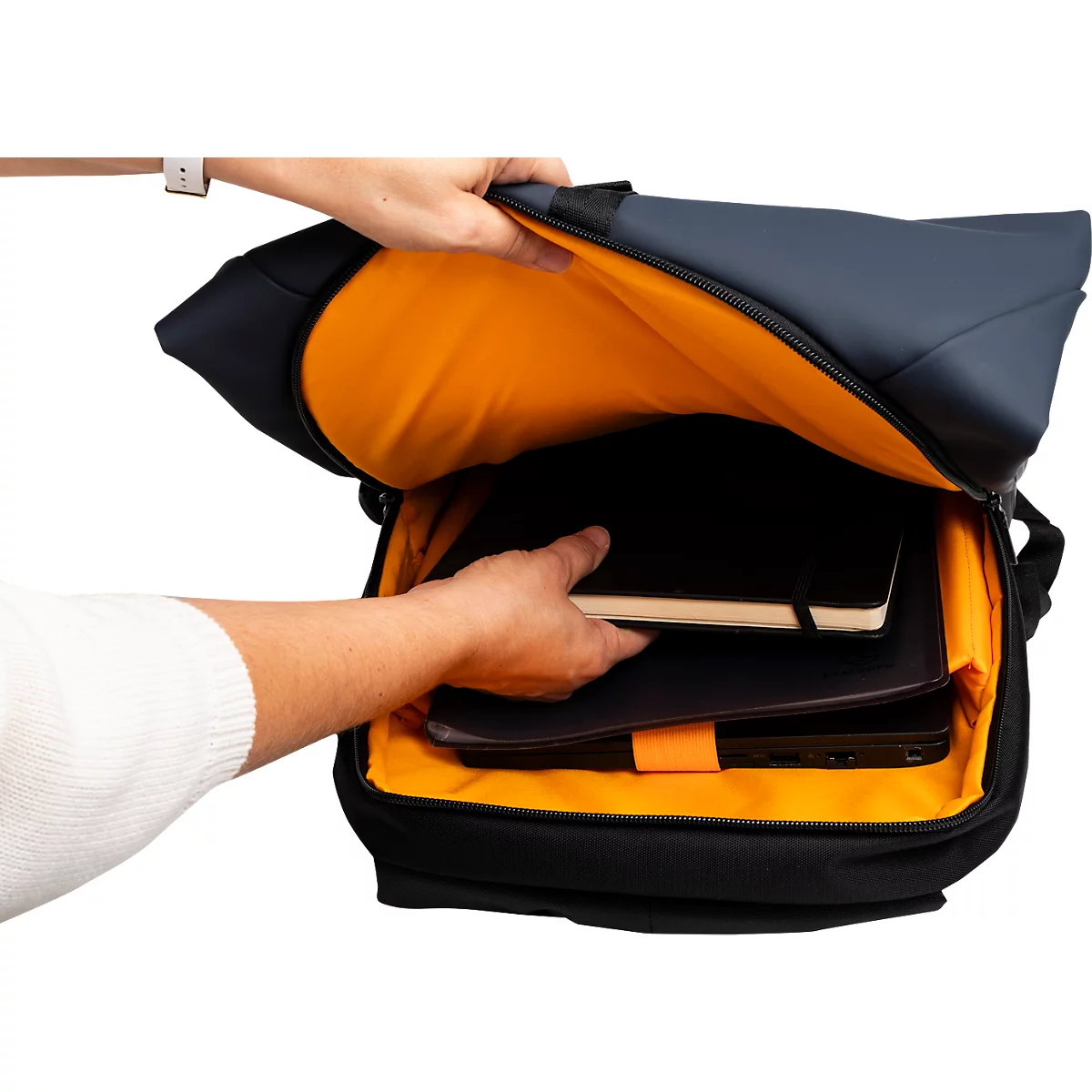 Eine Person öffnet einen schwarzen Rucksack mit orangenem Innenfutter, um Notizbuch und Laptop herauszunehmen.
