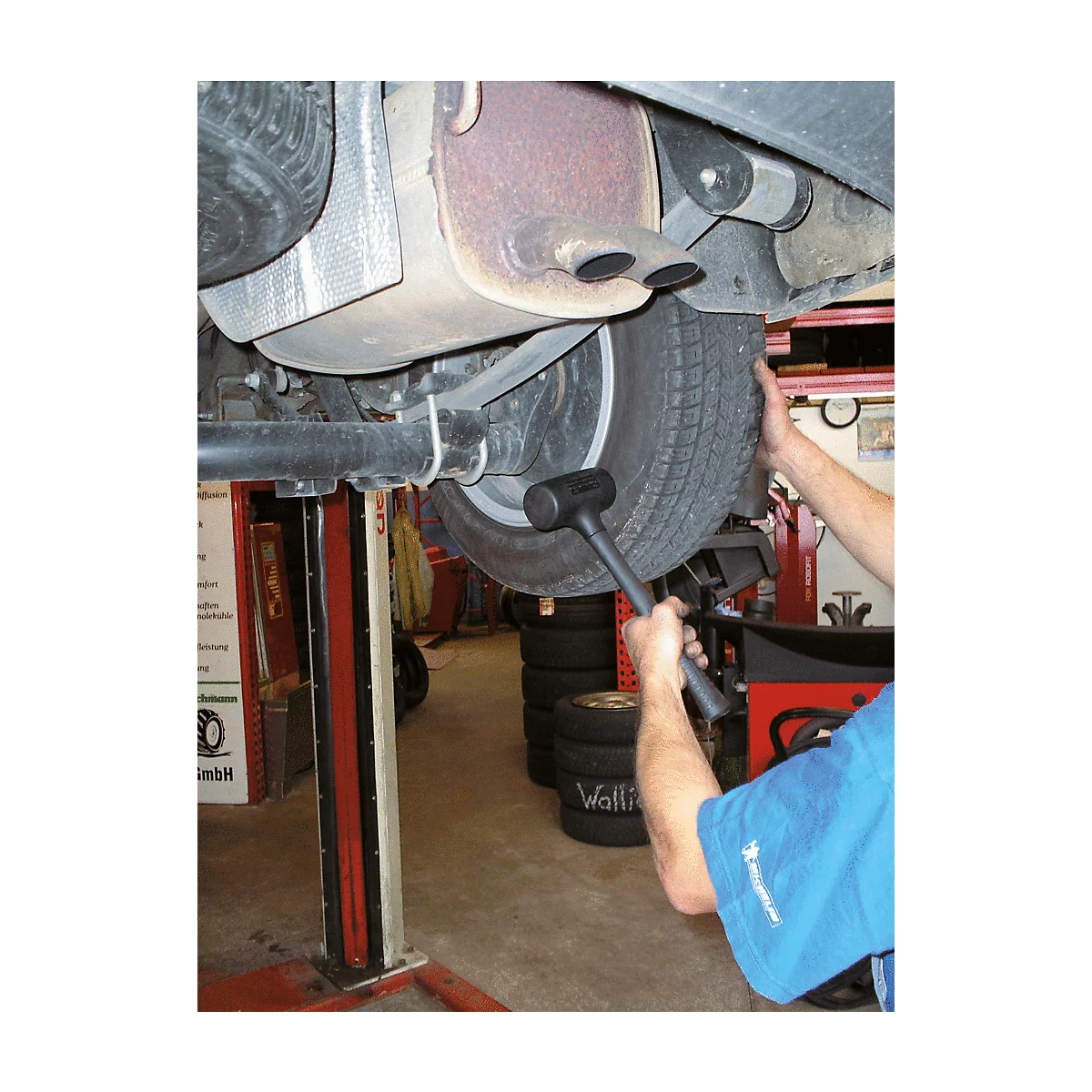 Ein Mechaniker schlägt mit einem Gummihammer auf einen Reifen, der an einem angehobenen Auto befestigt ist.