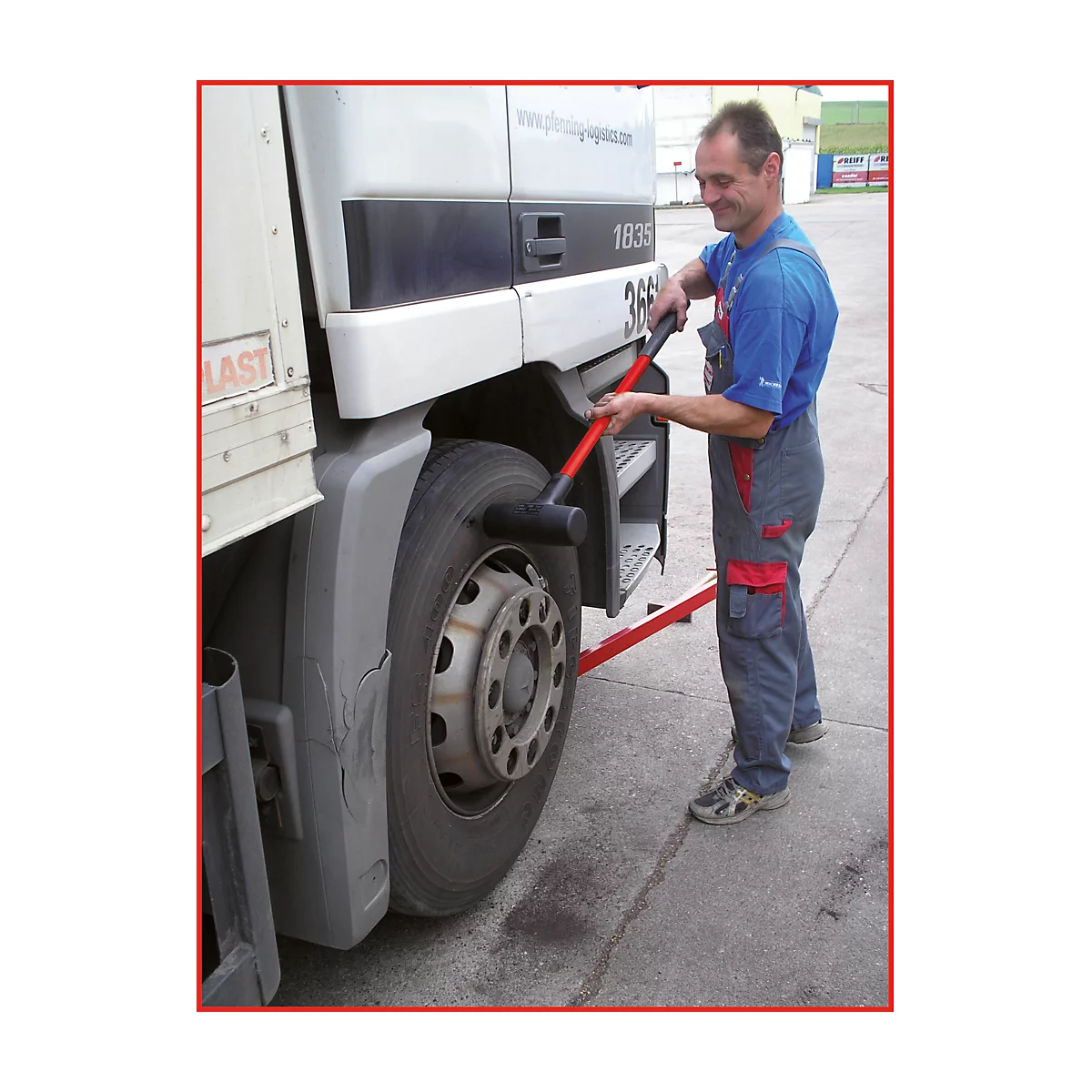 Ein Mann schlägt mit einem Hammer auf einen LKW-Reifen. Der Reifen steht auf einer roten Plattform.