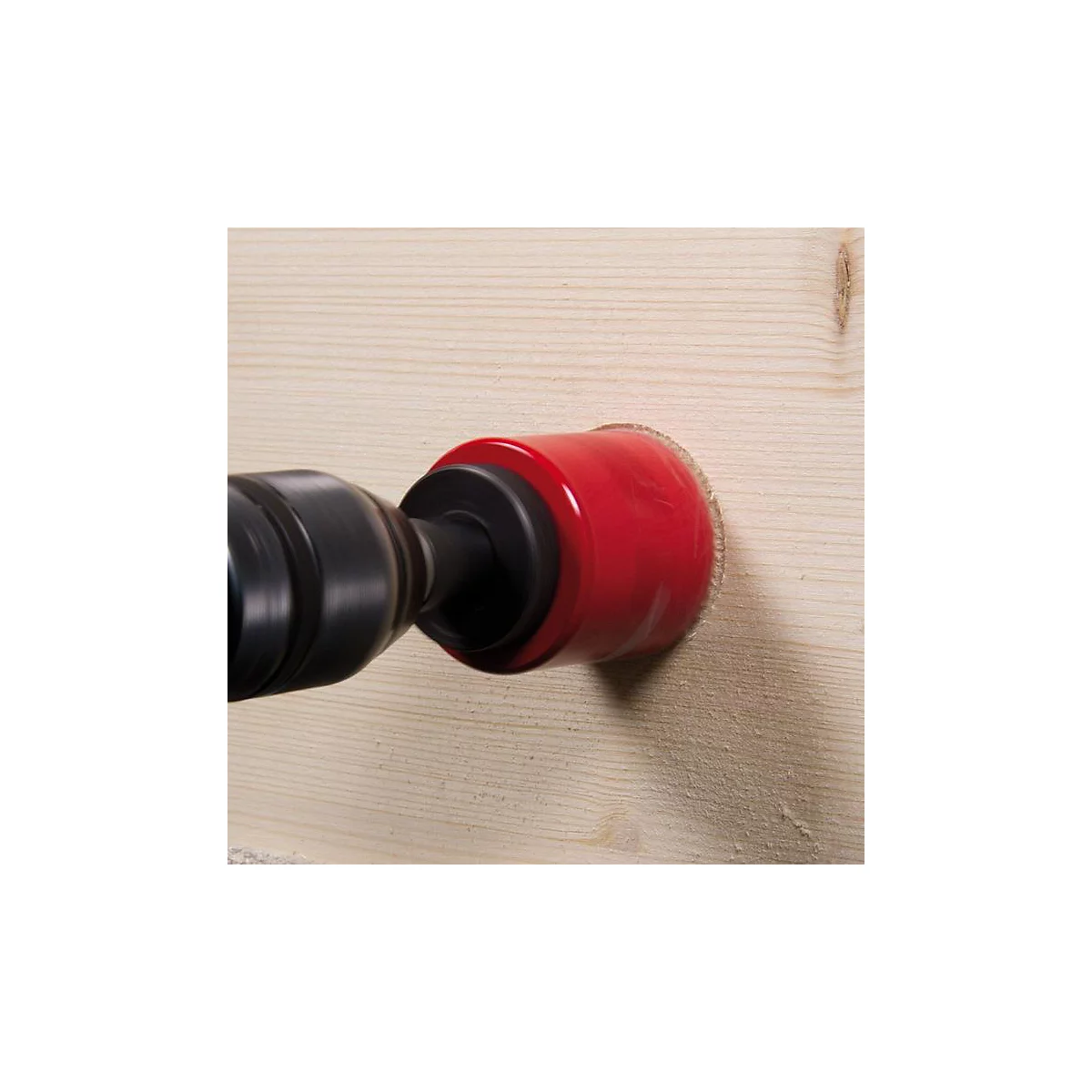 Een rode gatzagen boort een gat in een houten plank. De boor is in beweging.