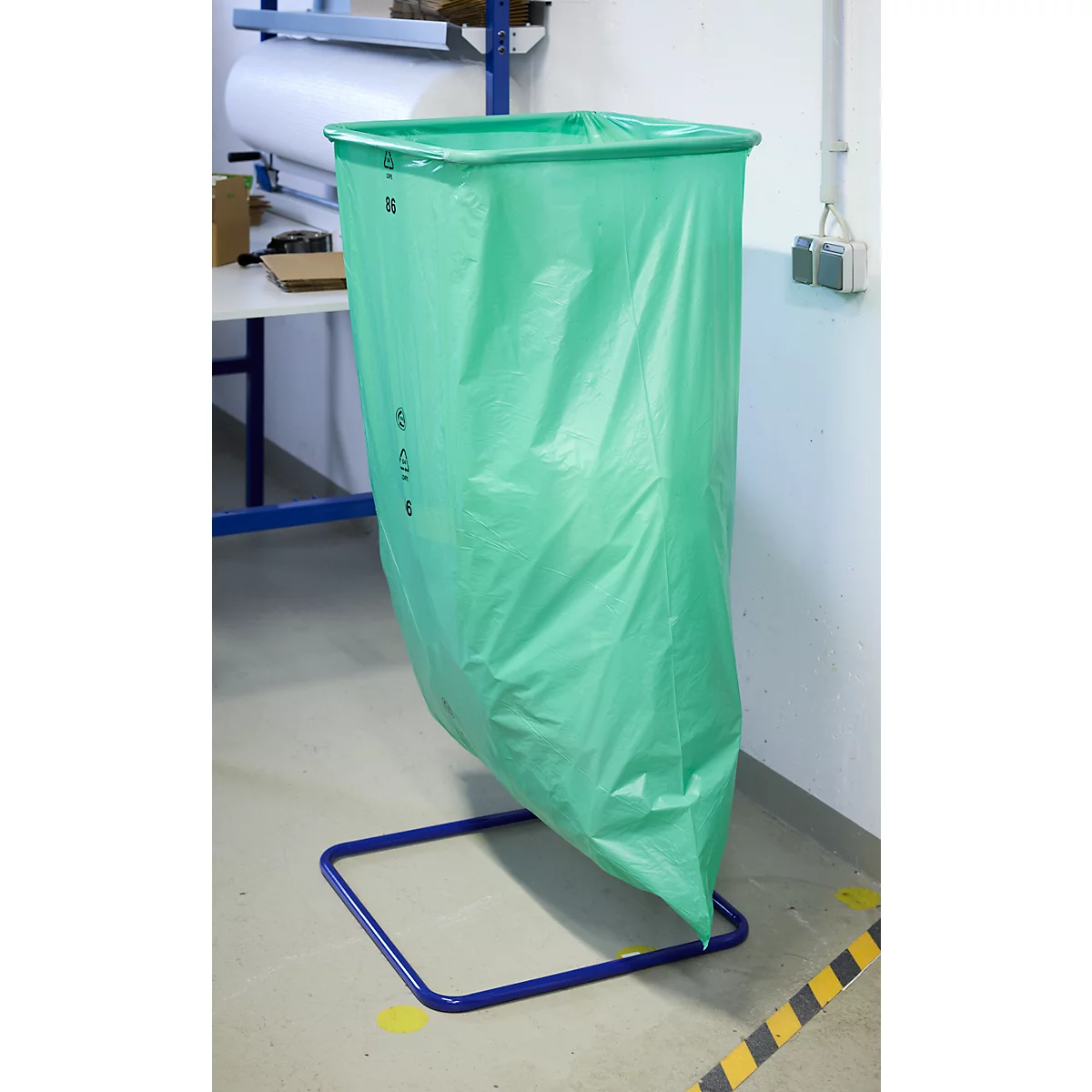 Un sac poubelle vert est posé sur un cadre bleu dans un entrepôt.