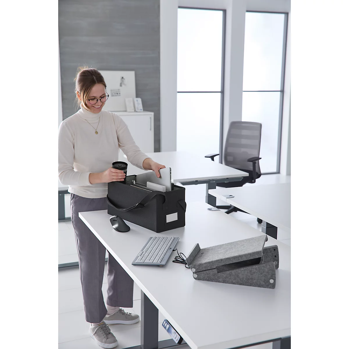 Femme portant des lunettes à son bureau. Elle met un ordinateur portable dans un sac noir.
