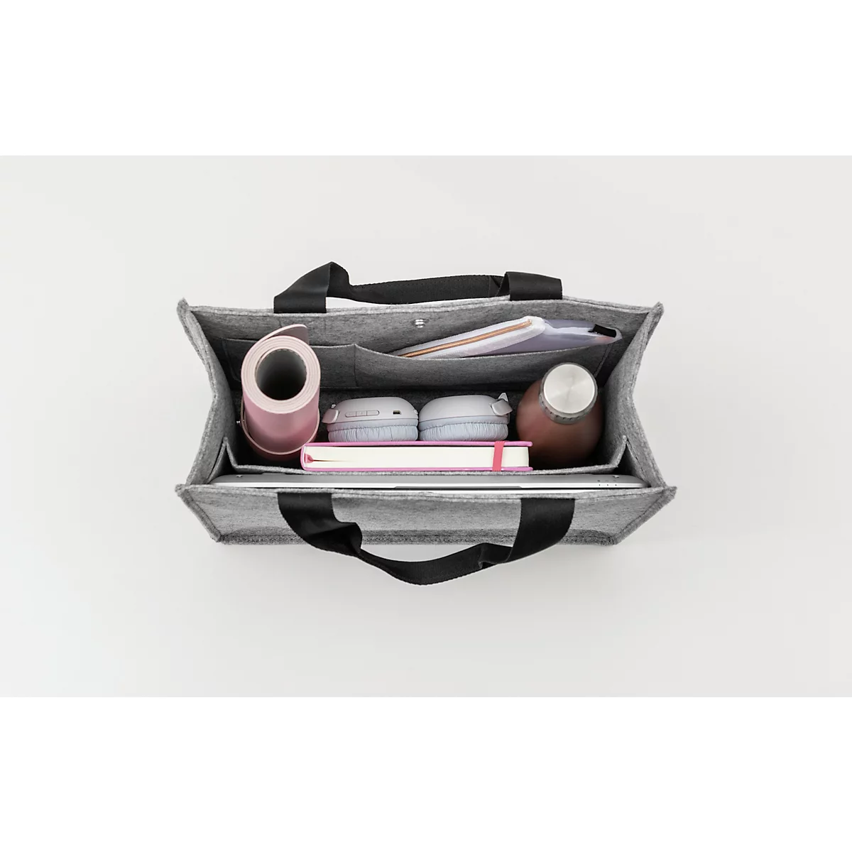 Sac en feutre gris avec contenu : tapis de yoga, écouteurs, carnet, bouteille d'eau. Poignées noires.