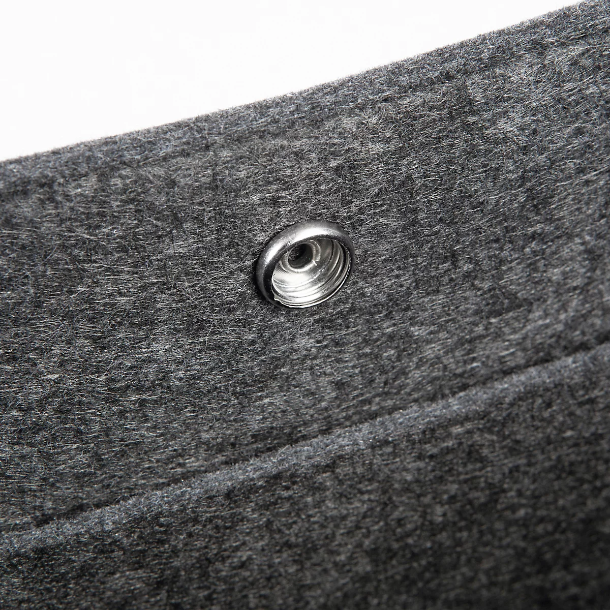 Gros plan sur une texture de feutre gris avec un bouton-pression argenté.