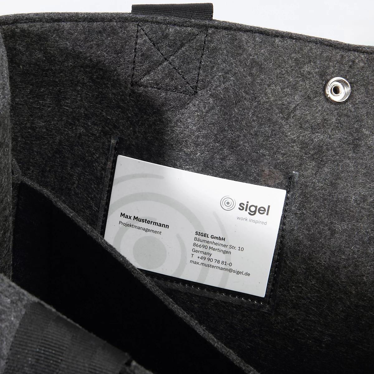 Gros plan d'un sac en feutre gris avec une étiquette nominative dans une poche intérieure.