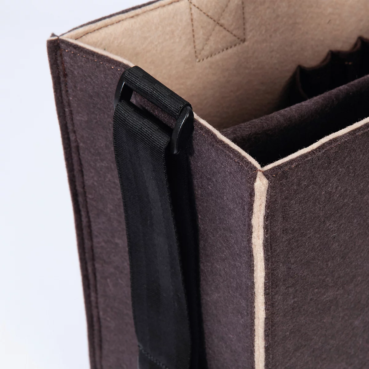 Gros plan sur un sac en feutre marron avec une bandoulière noire et une doublure beige.