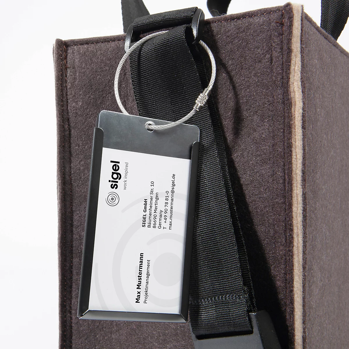 Sac en feutre gris-brun avec bandoulière noire. Une étiquette nominative de la société Sigel est attachée à un porte-clés.