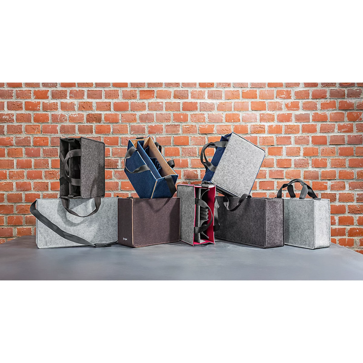 Une collection de sacs en feutre de différentes couleurs, devant un mur de briques rouges.