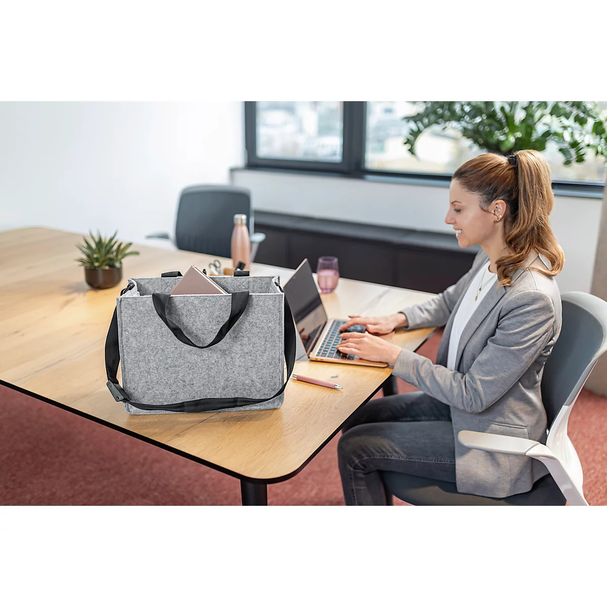 Une femme tape sur un ordinateur portable, un sac gris et un bloc-notes sont sur la table.