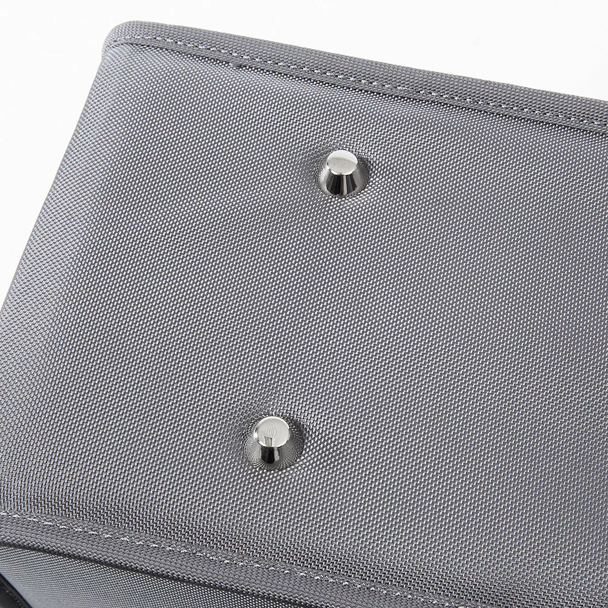 Gros plan sur un tissu gris avec deux rivets métalliques. Le tissu a une texture fine et est fini avec des coutures claires.