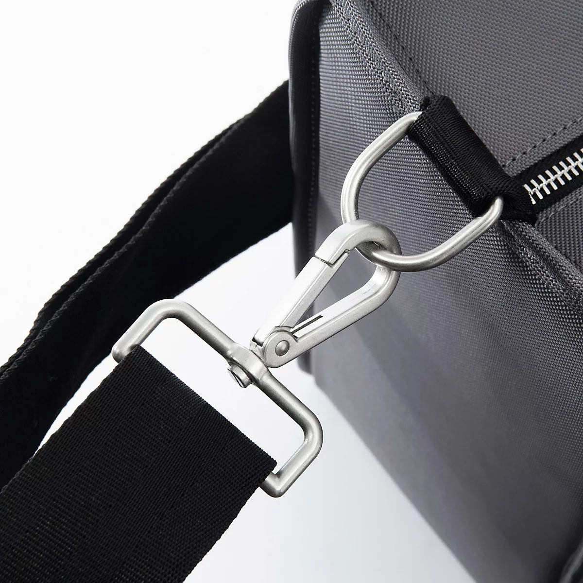 Gros plan d'un mousqueton argenté attaché à une bandoulière noire et à un sac gris.