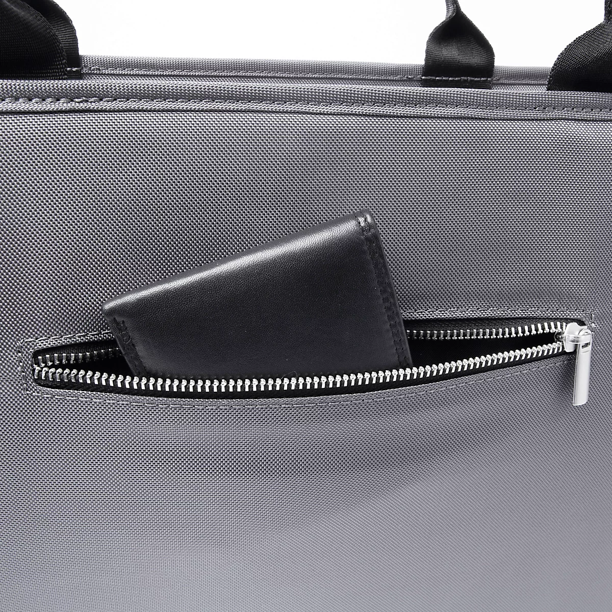 Portefeuille noir dans une poche zippée sur un sac à main gris.