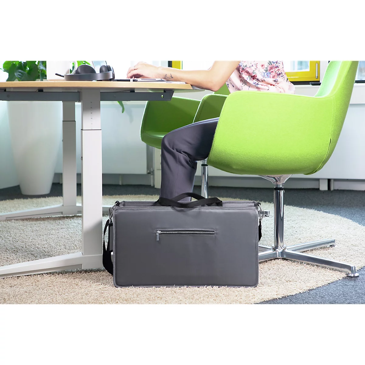 Personne au bureau avec un ordinateur portable et une chaise verte. Sac gris utilisé comme repose-pieds.