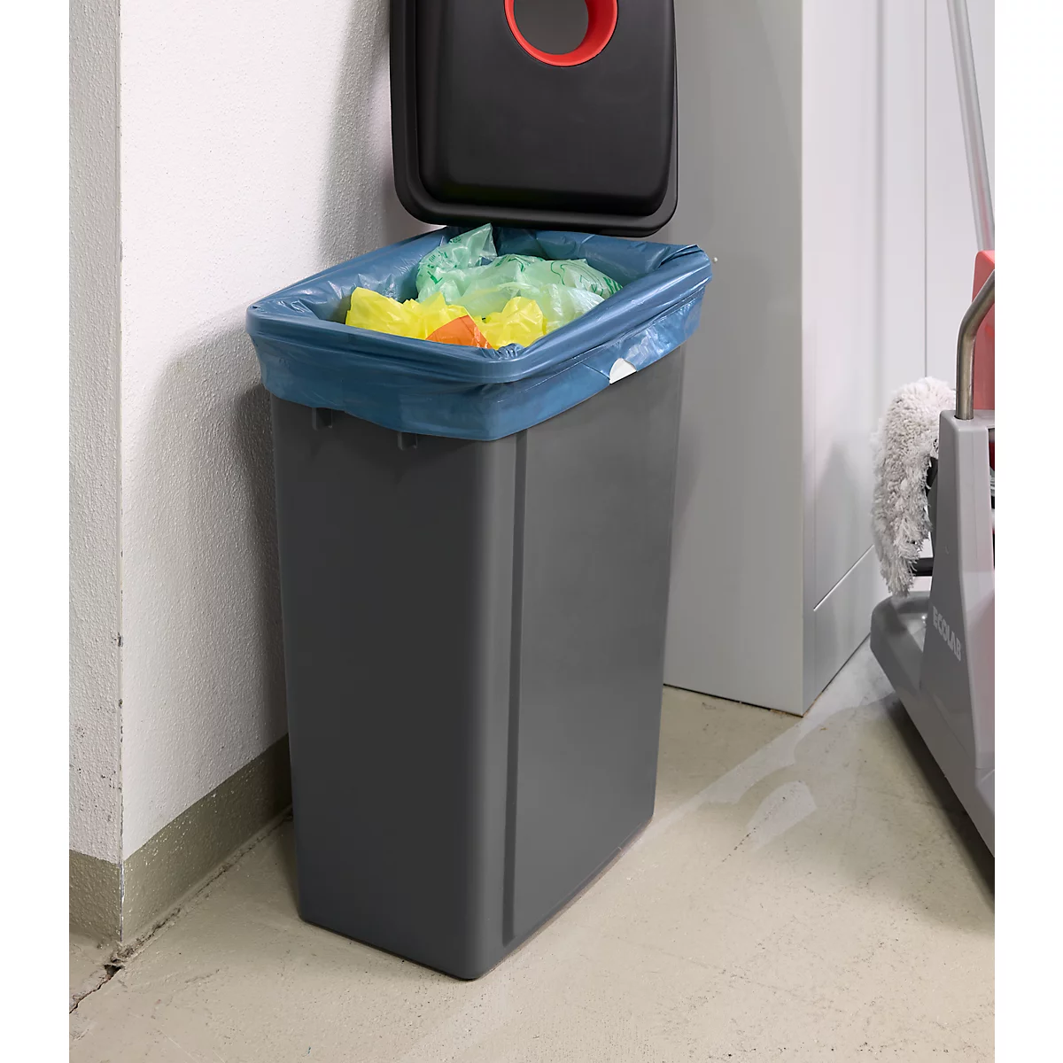 Poubelle grise avec couvercle ouvert, à l'intérieur un sac bleu rempli de déchets. Un cercle rouge est visible dans le couvercle.