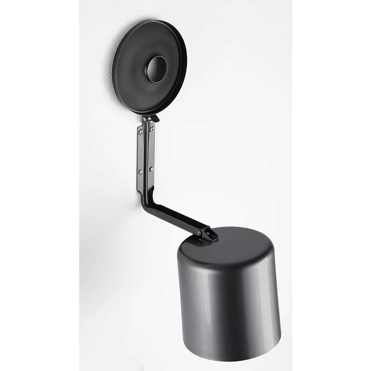 Black wall lamp, mounted on a white wall. Round base, cylindrical shade, angular arm. Minimalist design.