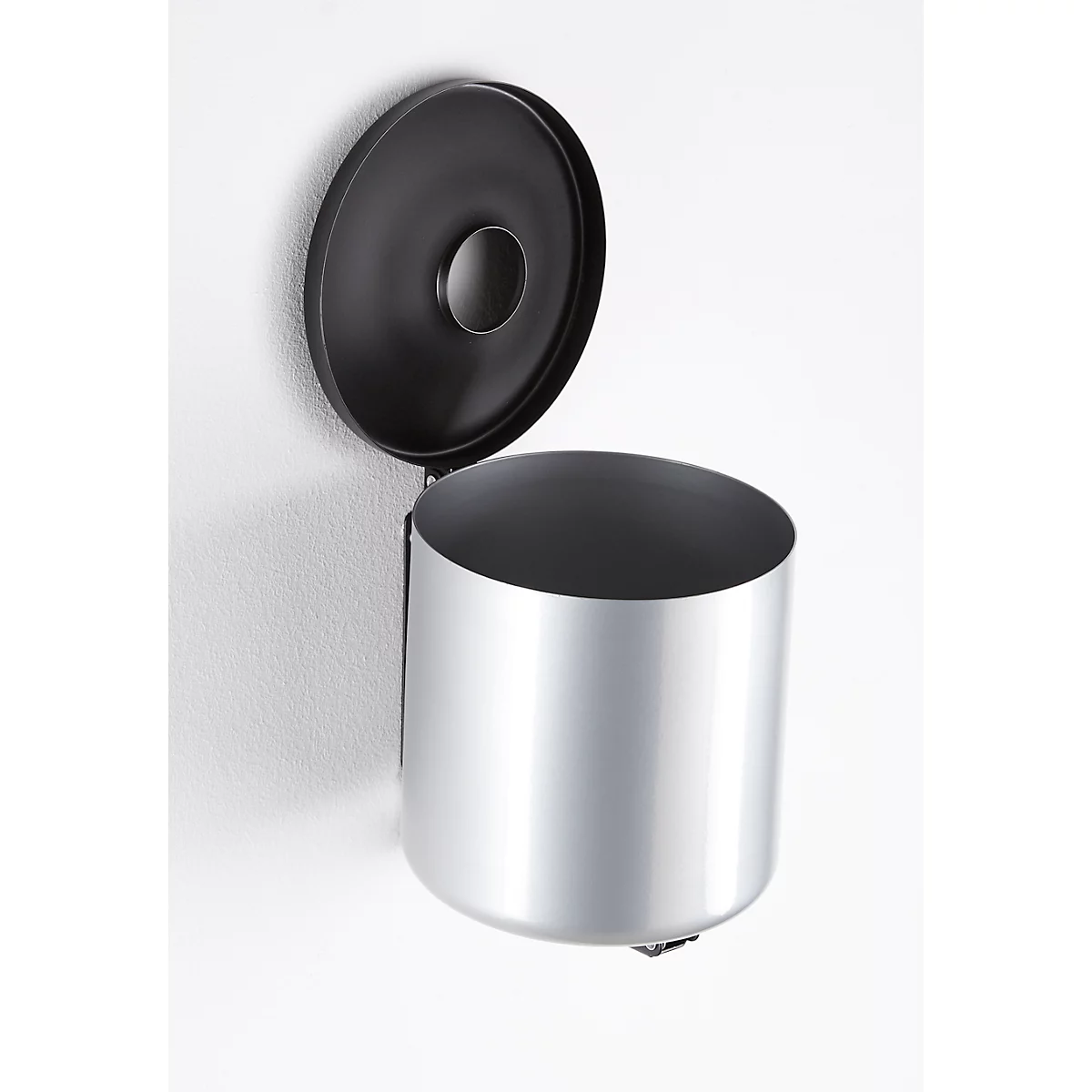 Silver wall-mounted waste bin with open black lid on white wall. The hole in the lid is visible.