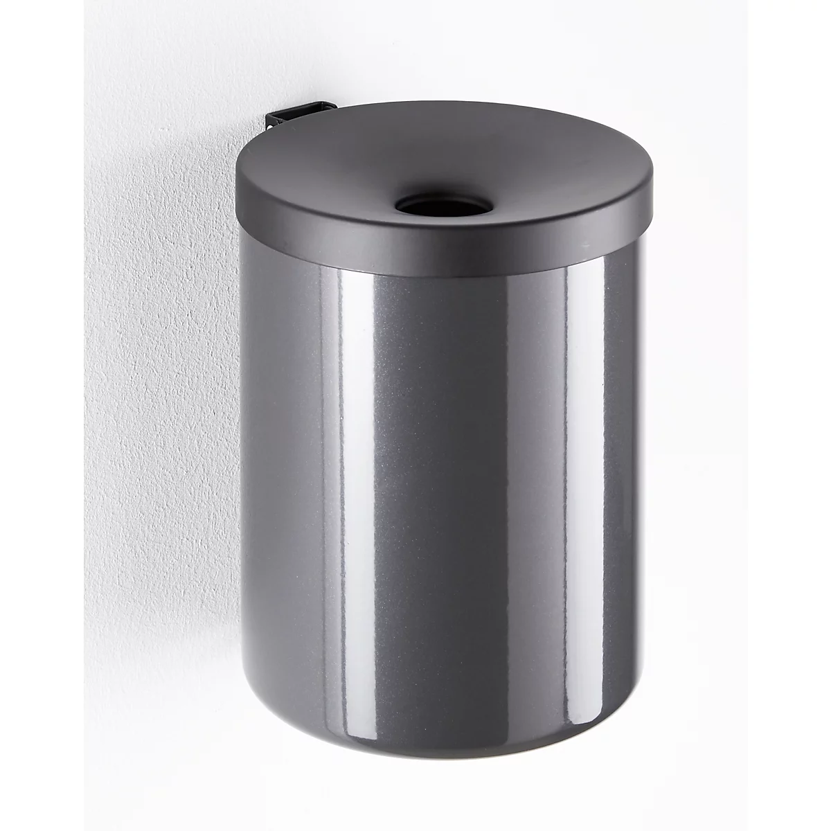 Gray, cylindrical trash can, attached to the wall. Lid with a circular opening.
