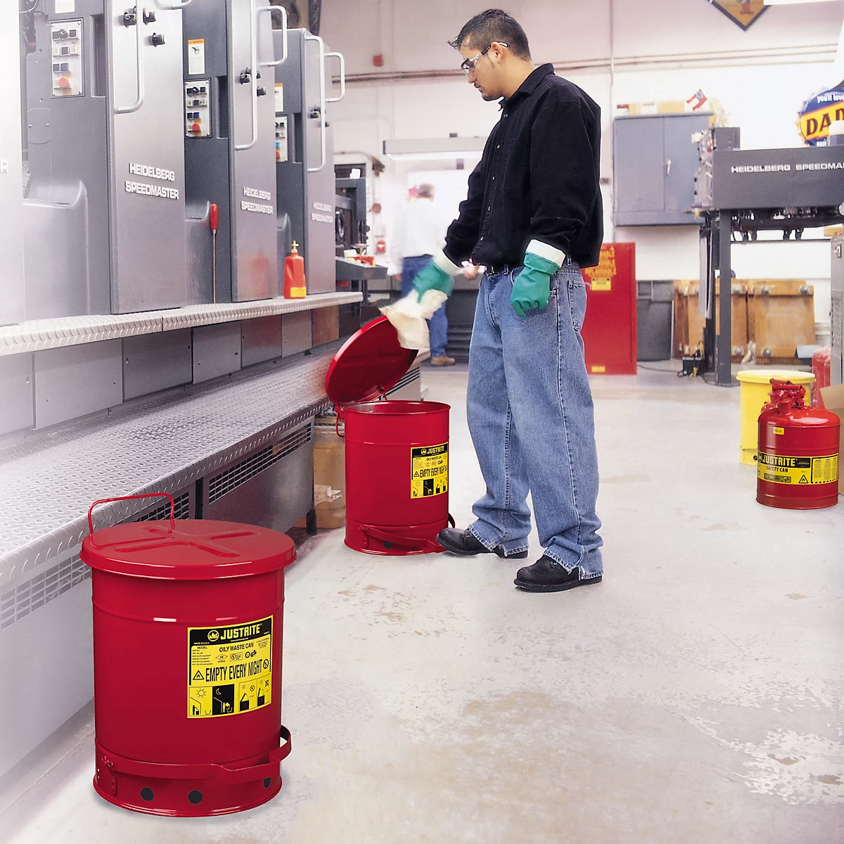 A man is disposing of waste in a red safety can. Another one stands next to it. Industrial environment.