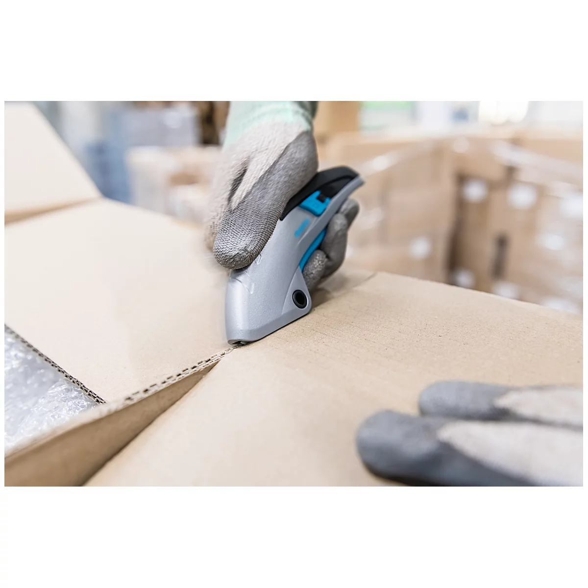 Person in gray gloves cutting open a cardboard box with a gray cutter.