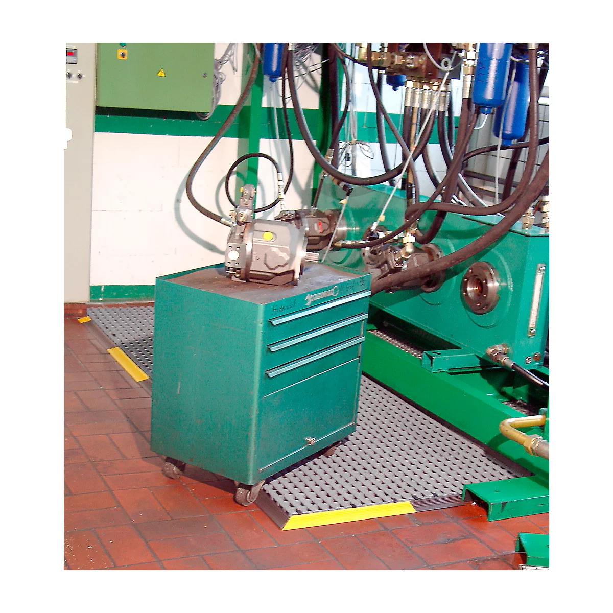 Green toolbox with wheels and mounted machine. In the background another machine and pipes.