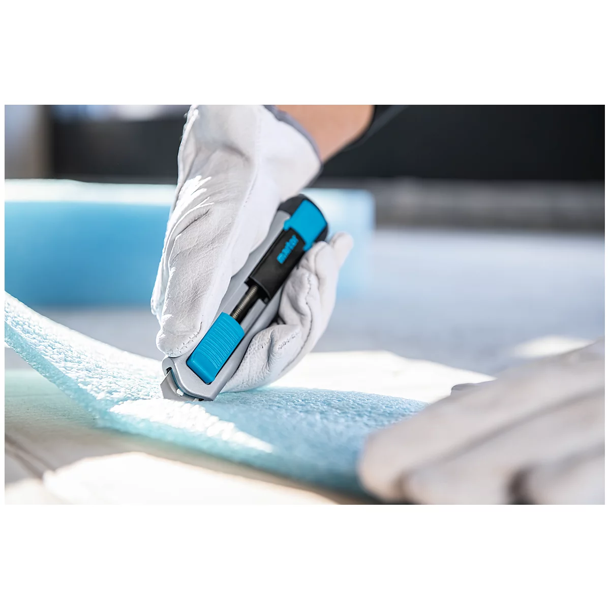 Person cuts blue foam material with a utility knife, gloves protect the hands.