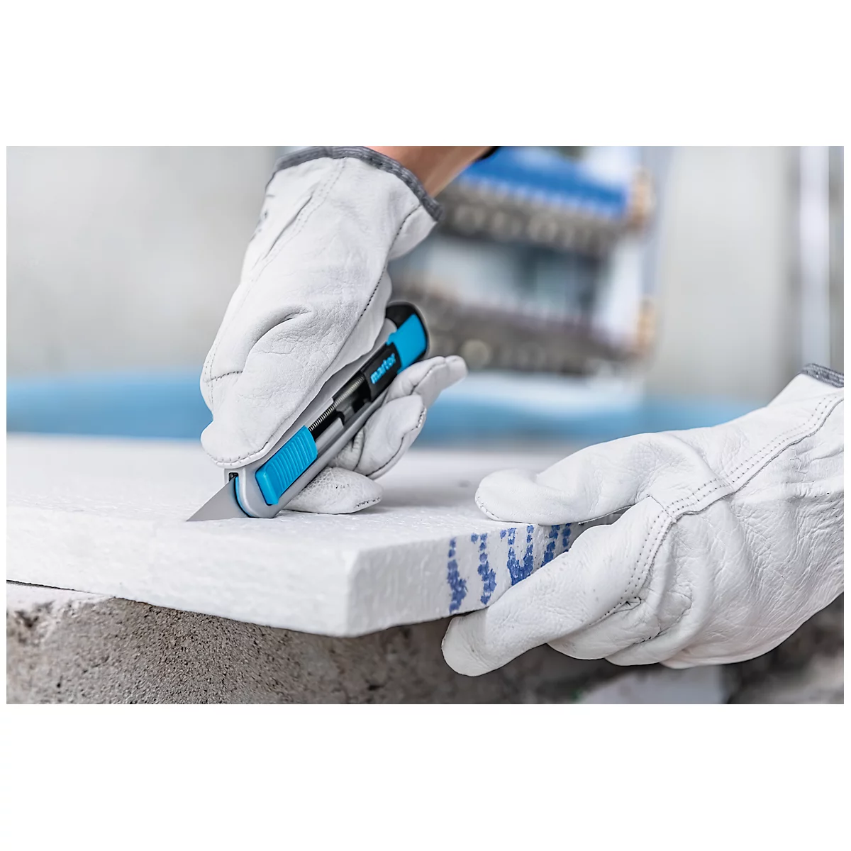 Person cutting an insulation board with a blue cutter, wearing white gloves.