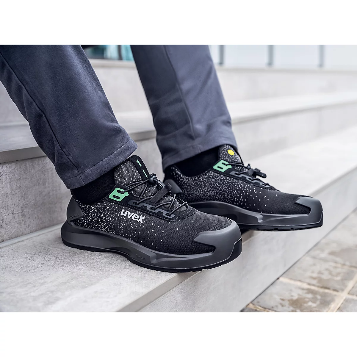 Black Uvex safety shoes on feet, sitting on a staircase.